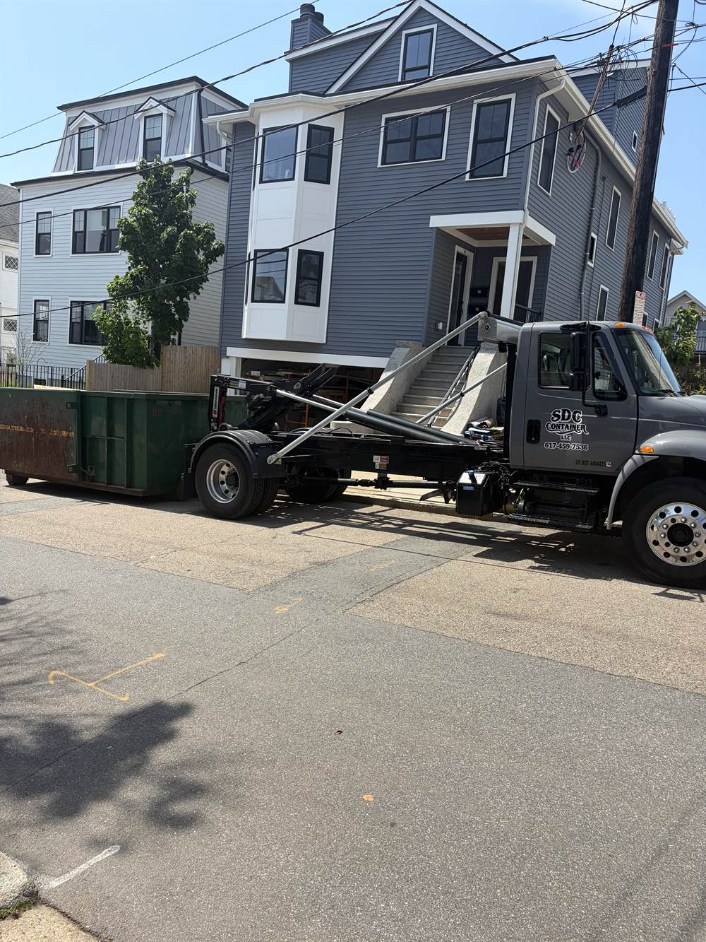 An SDC Container roll-off truck setting a container outside a three-storey home